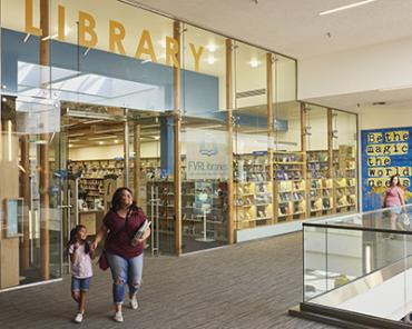 Adult holds hand of child as they pass by the Vancouver Mall Library's entrance