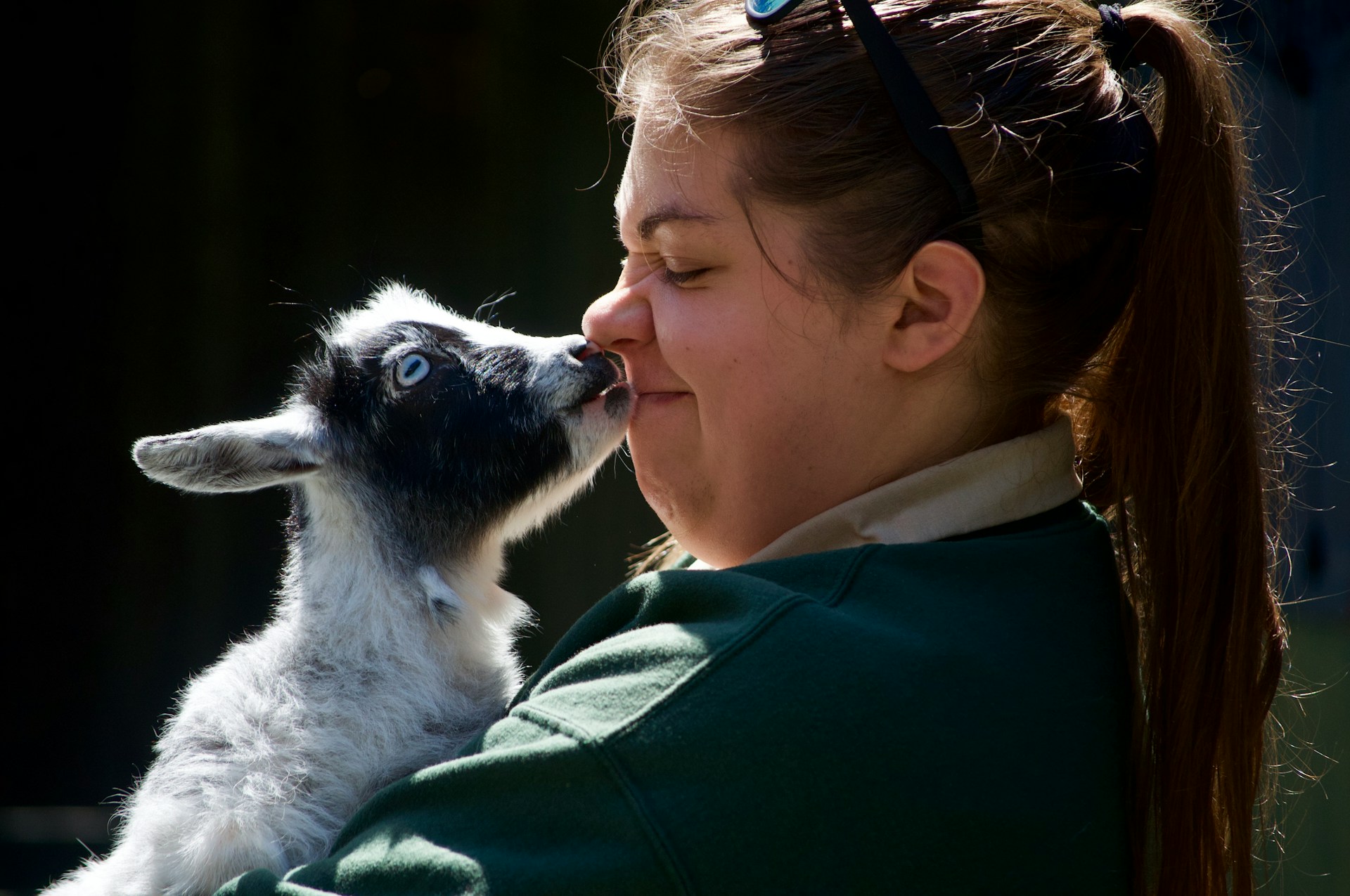 Woman in a green jacket holds a black and white goat