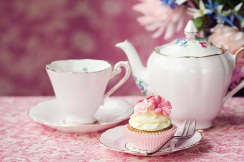 image of a tea set and cupcake with a floral pink background