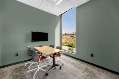 Small room with sage green walls and floor-to-ceiling window with table, chairs, and digital viewing screen