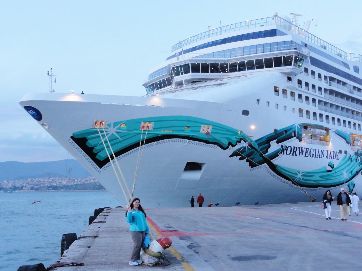 Woman standing on a dock in front of the Norwegian Jade Cruise ship.